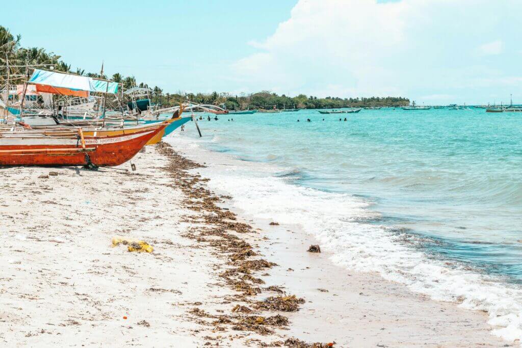 Serene tropical beach with traditional boats, inviting turquoise seawater and soft sandy shore.