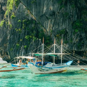 Traditional outrigger boats float by majestic limestone cliffs in turquoise waters, ideal for travel and touri