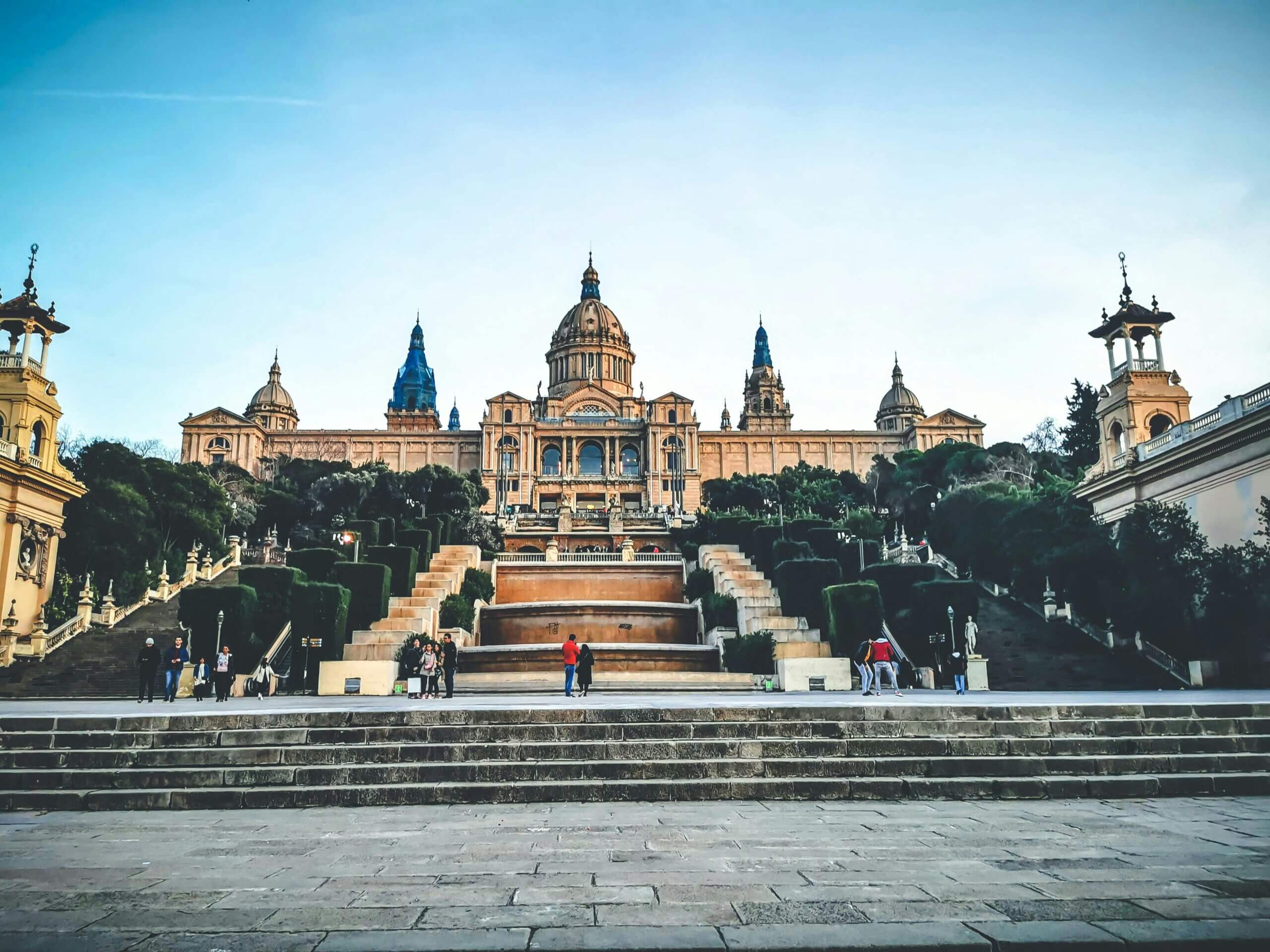 Exterior of historic National Art Museum of Catalonia with dome and spires surrounded with lush gardens and ta