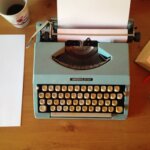 Classic blue typewriter on a wooden desk with paper, pen, and notepad, evoking vintage nostalgia.