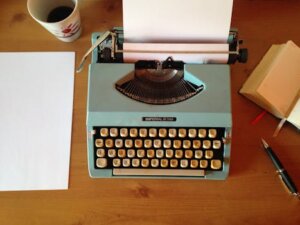 Classic blue typewriter on a wooden desk with paper, pen, and notepad, evoking vintage nostalgia.