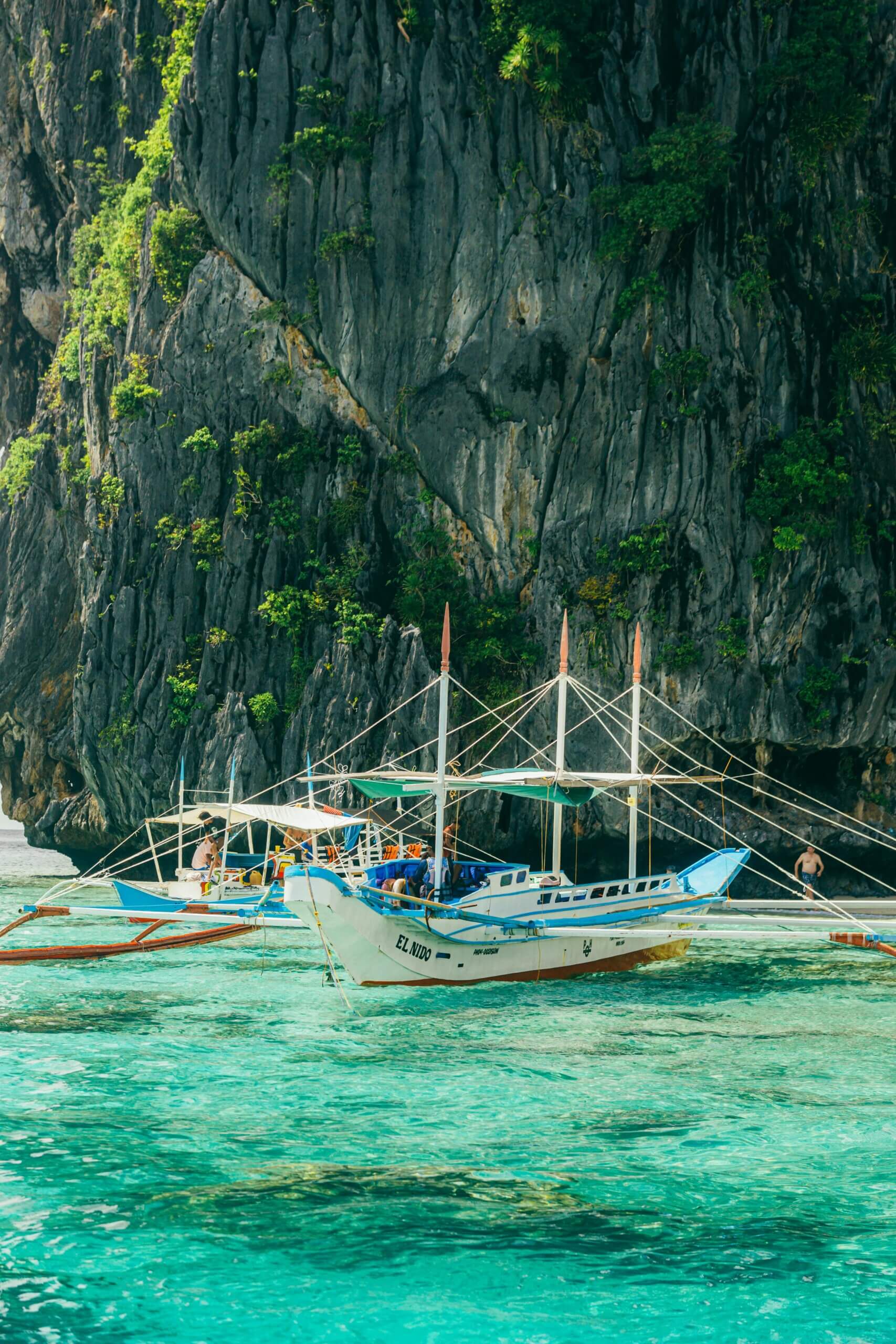 Traditional outrigger boats float by majestic limestone cliffs in turquoise waters, ideal for travel and tourism themes.